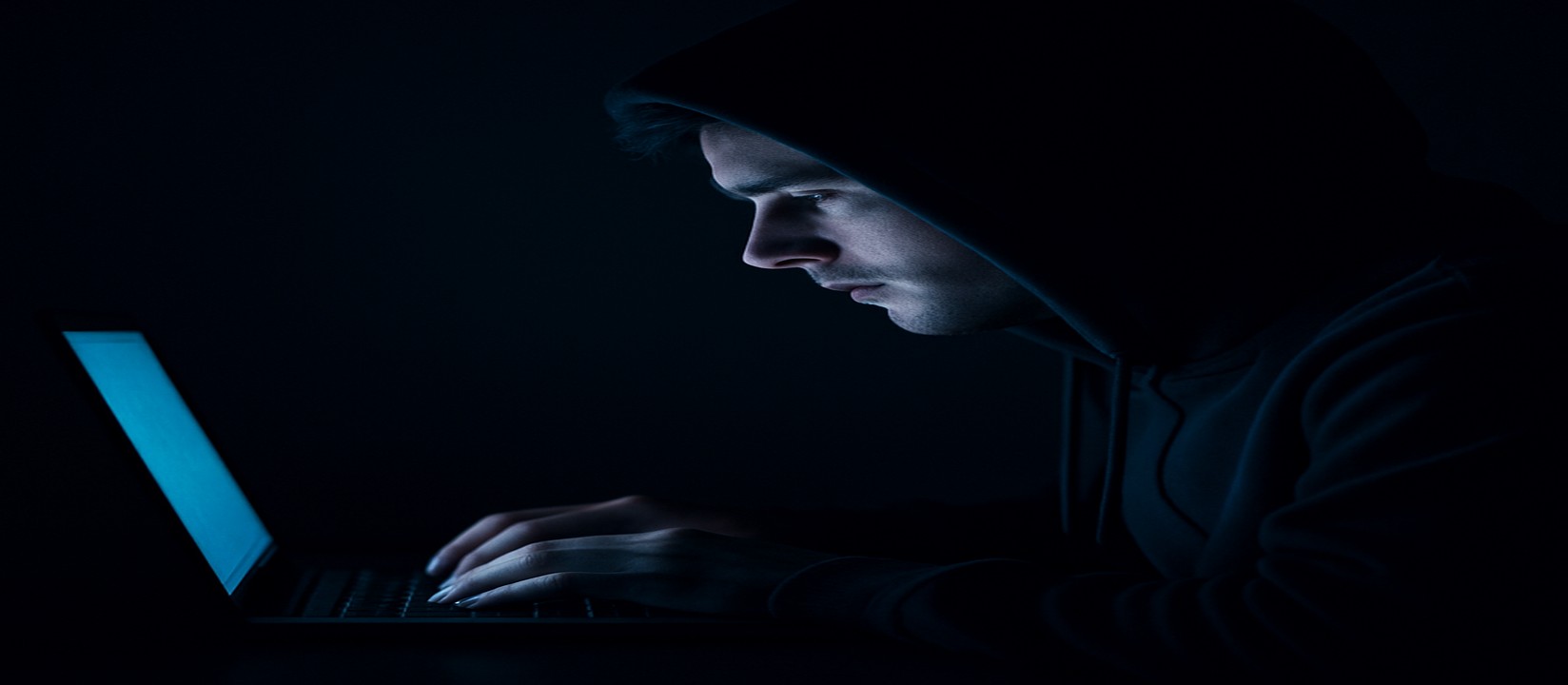 একজন ব্যক্তি অন্ধকারে ল্যাপটপে বসে মনোযোগী চেহারা নিয়ে kiriya ওয়েবসাইটে অনলাইন গেম খেলছেন